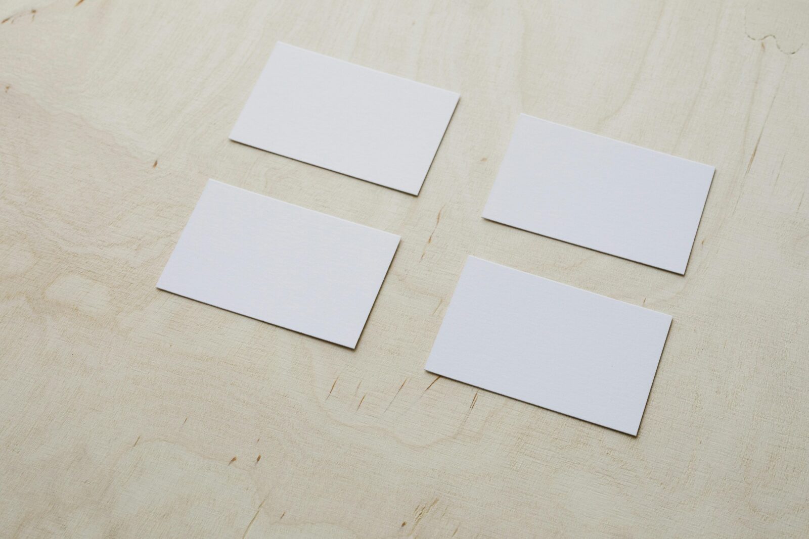 Four blank business cards arranged neatly on a light wooden background, perfect for branding presentations.