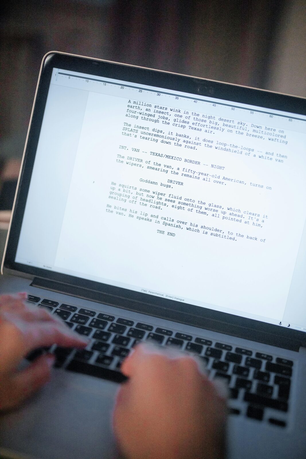 Close-up of hands typing a screenplay on a laptop, showcasing digital writing.